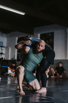 two men wrestling in a gym with one holding the other's head while another squats behind him