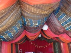 the inside of a tent with curtains and lights on it's ceiling is decorated in bright colors