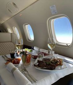 an airplane meal with wine and food on the table in front of two large windows