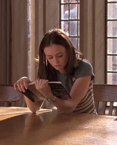 a woman sitting at a table with a book in her hand and looking down on the floor