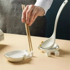 a person holding two chopsticks in front of a bowl and spoon on a table