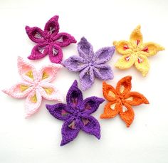 six crocheted flowers are arranged on a white surface, each with different colors