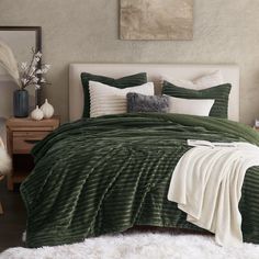 a bed with green comforter and pillows in a room next to a painting on the wall