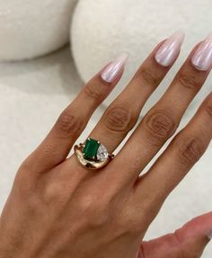 a woman's hand holding a ring with an emerald and diamond on the middle