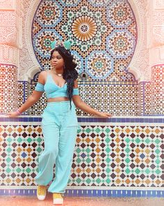 a woman standing in front of a wall with colorful tiles on it and her arms spread out