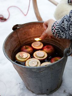 a person is lighting candles in a bucket filled with water and apples on the snow