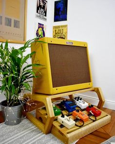 a yellow amp sitting on top of a wooden stand next to a potted plant