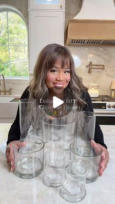 a woman standing in front of a stack of glasses on top of a kitchen counter