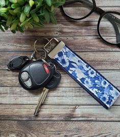 a keychain, glasses and keys on a wooden table next to a potted plant