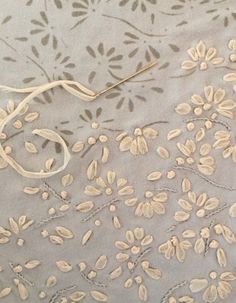 an embroidered fabric with white flowers and leaves on it, next to a pair of scissors