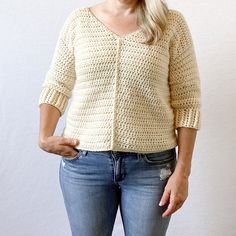 a woman with blonde hair wearing jeans and a white knitted sweater is posing for the camera