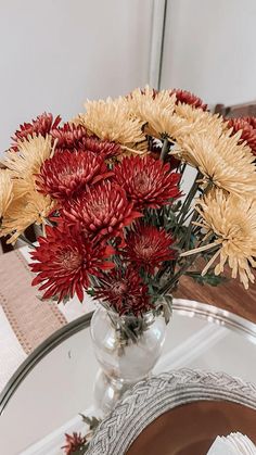 a vase filled with red and yellow flowers on top of a glass table next to a mirror