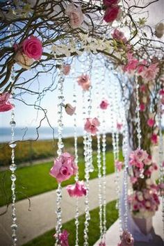 an outdoor wedding with pink flowers and beads hanging from the branches, along with greenery