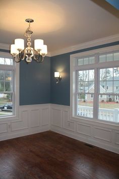 an empty living room with blue walls and wood floors, chandelier hanging from the ceiling