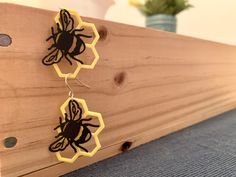 two wooden earrings with black and yellow designs hanging from hooks on a piece of wood