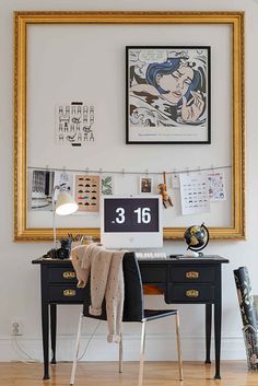 a desk with a computer on top of it in front of a painting and pictures