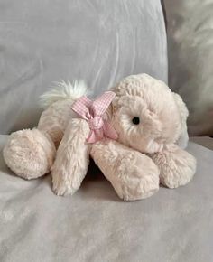 a white teddy bear with a pink bow sitting on a couch in front of pillows