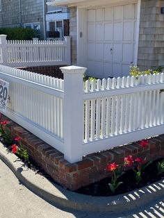 a white picket fence in front of a house with flowers growing on the side walk