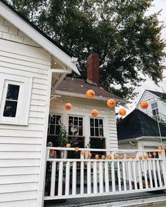 halloween decorations on the front porch of a white house with pumpkins hanging from it