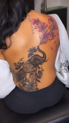 the back of a woman's body with an elephant and flowers tattoo on it