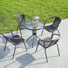 four chairs and a table on the ground in front of some grass with a flower