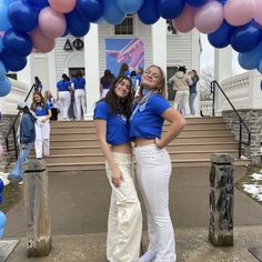 two women standing in front of a building with blue and pink balloons