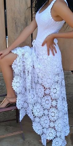 a woman is sitting on a chair wearing a white crochet dress and sandals