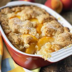 a peach cobbler in a red casserole dish on a yellow and white towel