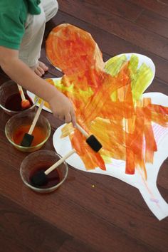 a child is painting a paper turkey on the floor