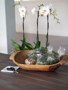 two white orchids in a wooden bowl on a table with plastic wrap and scissors