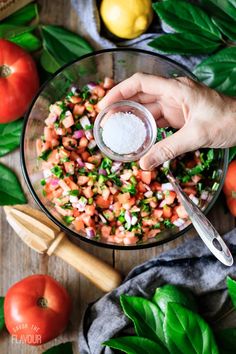 someone is adding seasoning to a salad in a glass bowl with tomatoes and basil