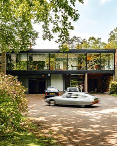 an old car is parked in front of a modern house with glass walls and large windows