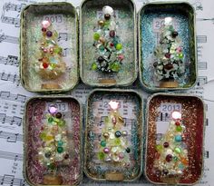 four tin canisters with christmas trees in them on top of sheet music paper