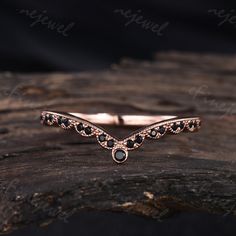 a rose gold ring with black diamonds on it sitting on top of a piece of wood