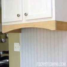 a kitchen with white cabinets and wood trim on the wall above it is an empty chair