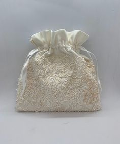 a white lace bag with a satin bow on the front and side, sitting against a white background