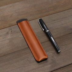 a pen sitting on top of a wooden table next to a leather case