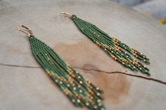 a pair of green beaded earrings sitting on top of a piece of wood with beads hanging from it