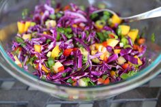 a glass bowl filled with coleslaw, carrots and green onions next to a metal spoon