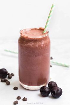 a smoothie in a glass with a green and white striped straw next to some raisins