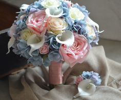 a bridal bouquet with pink, blue and white flowers on a cloth draped table