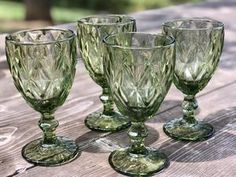 four green glass goblets sitting on top of a wooden table