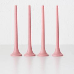 three pink candles sitting next to each other on top of a white table with a wall in the background