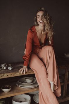 a woman sitting on top of a wooden table next to white bowls and plates in a room