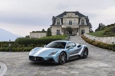 a blue sports car is parked in front of a large house on a cobblestone driveway