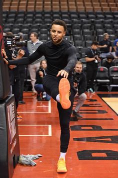 a man in black shirt and orange shoes doing tricks on basketball court with people watching