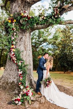 a bride and groom standing under a large tree with flowers on it's branches