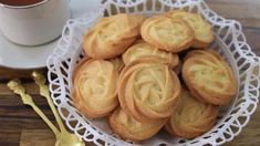 some cookies are on a white plate next to a cup of tea and gold spoons