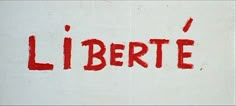 the word libertte is painted on a white wall with red spray paint over it