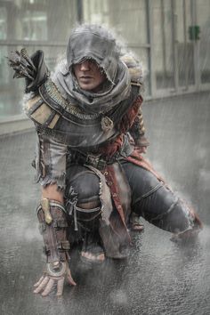 a man dressed in armor crouching down on the ground with an umbrella over his head